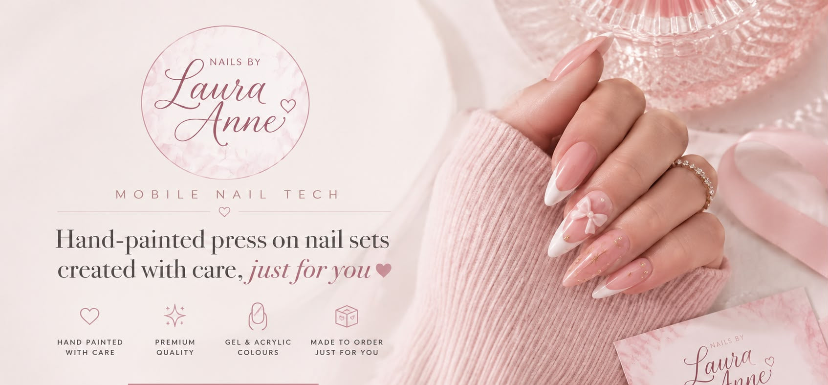 A close-up of a hand with long, neatly manicured press-on nails in a pale pink and white floral design, resting on a soft pink knit sleeve. The background is a soft pink with branding for 'Laura Anne Mobile Nail Tech' and a small matching card.